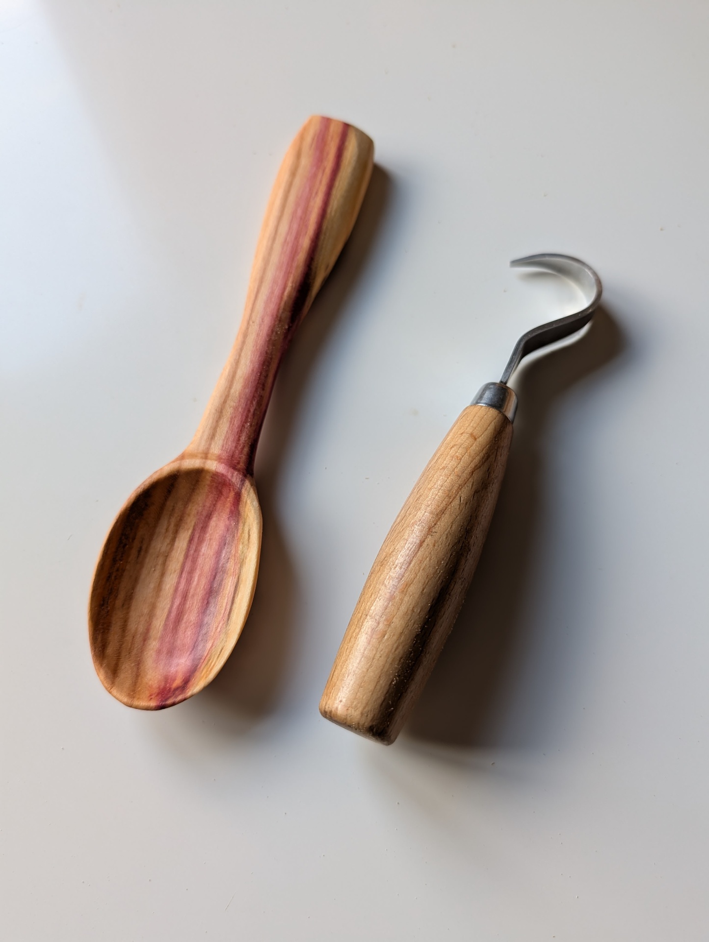 Freshly carved cherry wood spoon beside a hook knife carving tool
