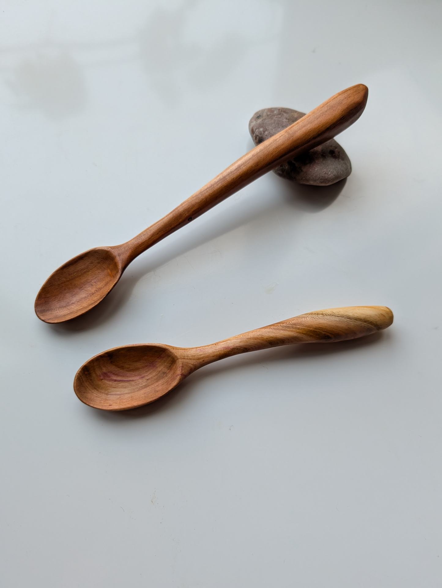 Pair of small wooden tasting spoons resting on river stones