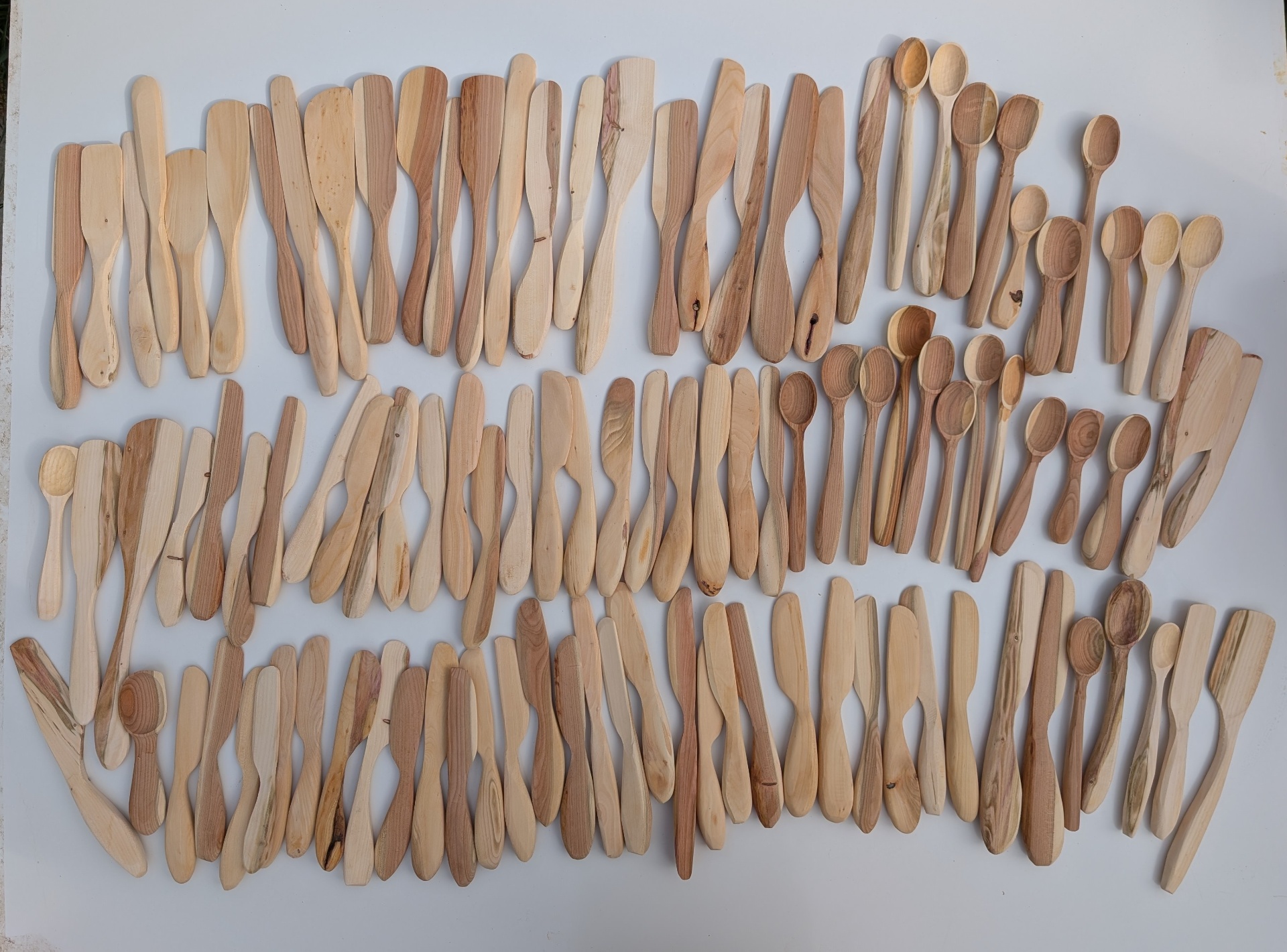 Large batch of hand-carved wooden spatulas, butter knives and spoons laid out in rows